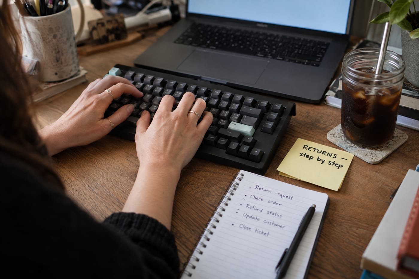 Hands typing at a keyboard beside a handwritten sticky note outlining a returns process